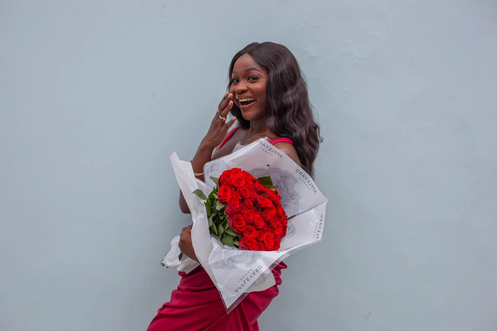 Model Grace smiling with red roses against a blue wall, model book